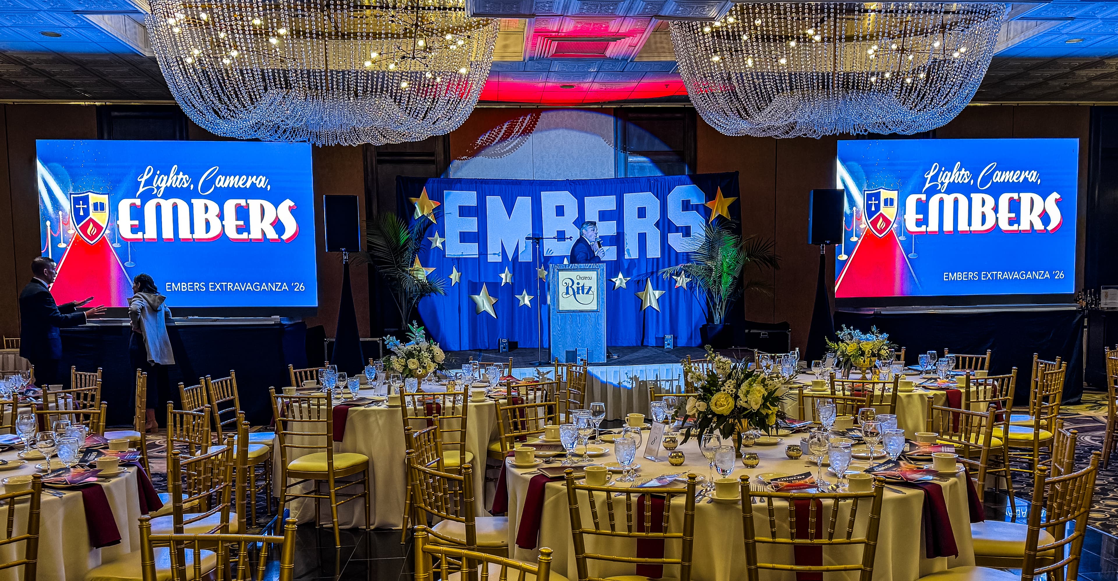 Elegant ballroom with crystal chandeliers and set tables for the 'Lights, Camera, Embers' gala.