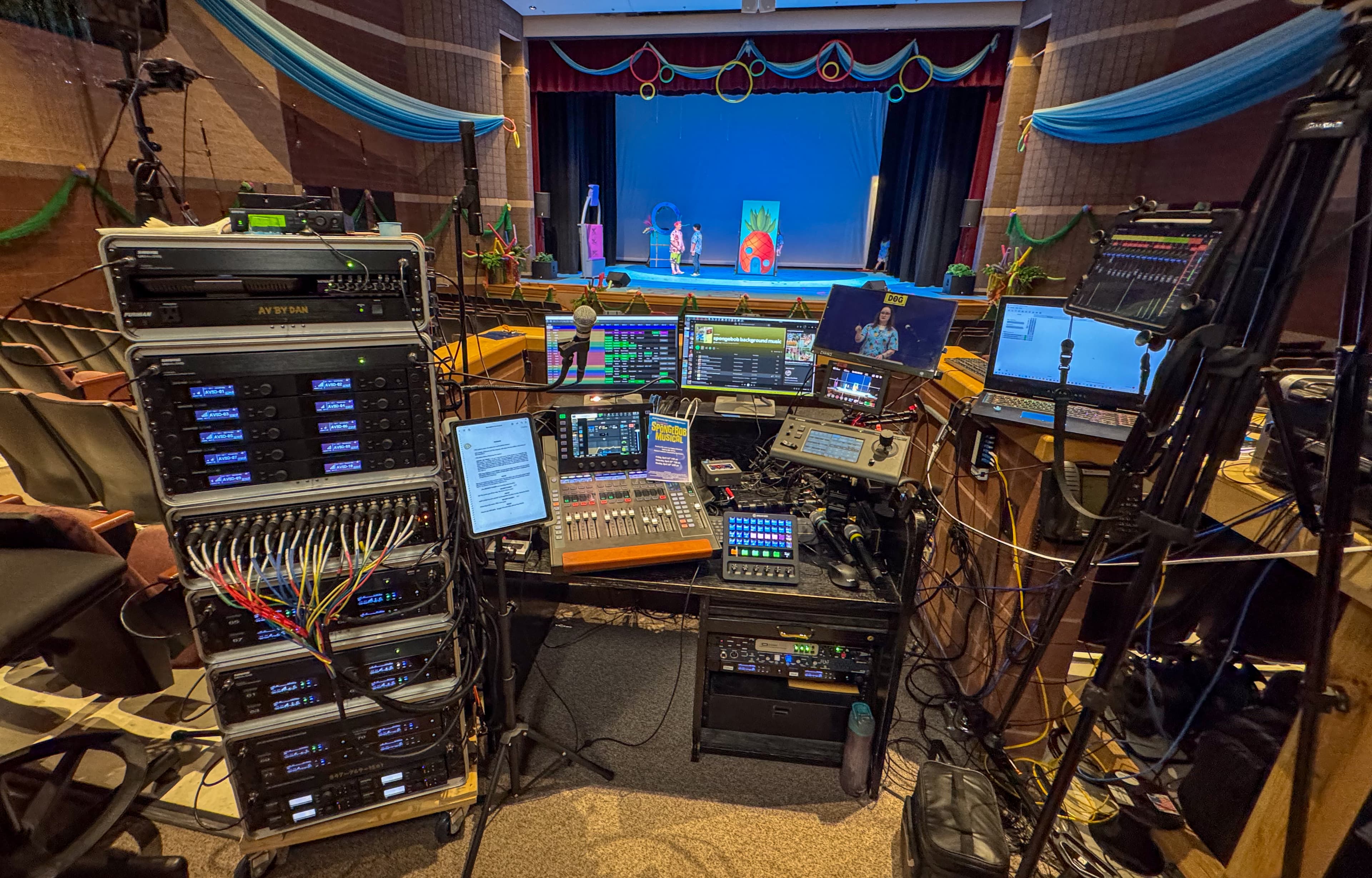 Professional audio-visual control booth with monitors and mixing boards overlooking a live theater stage performance.